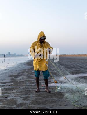 karachi pakistan 2021, un pêcheur portant une veste jaune préparant un filet de pêche pour la pêche en vue de la mer en soirée. Banque D'Images