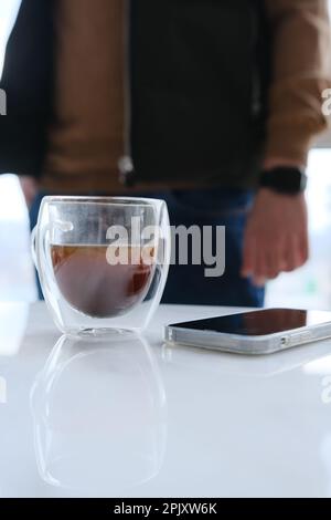 homme d'affaires buvant du café, une tasse de café transparente sur un bureau en marbre blanc, ayant des pauses, des pensées profondes, appréciant la vue, attendant la réunion à Banque D'Images