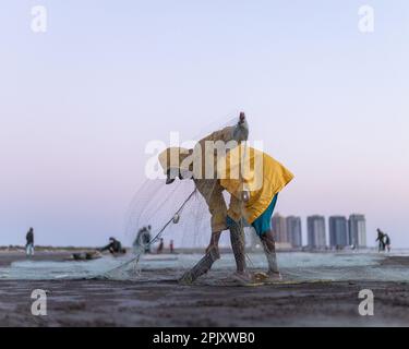 karachi pakistan 2021, un pêcheur portant une veste jaune préparant un filet de pêche pour la pêche en vue de la mer en soirée. Banque D'Images