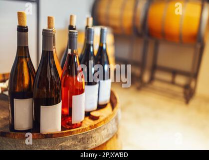 Gros plan de la maquette d'un groupe de bouteilles de verre avec différents vins et champagne sur baril de vin en bois. Vider les autocollants blancs sur les bouteilles. Espace libre pour Banque D'Images