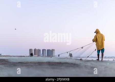 karachi pakistan 2021, un pêcheur portant une veste jaune préparant un filet de pêche pour la pêche en vue de la mer en soirée. Banque D'Images