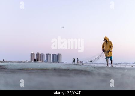 karachi pakistan 2021, un pêcheur portant une veste jaune préparant un filet de pêche pour la pêche en vue de la mer en soirée. Banque D'Images