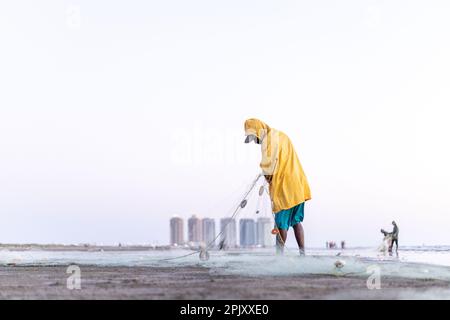 karachi pakistan 2021, un pêcheur portant une veste jaune préparant un filet de pêche pour la pêche en vue de la mer en soirée. Banque D'Images