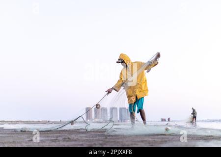 karachi pakistan 2021, un pêcheur portant une veste jaune préparant un filet de pêche pour la pêche en vue de la mer en soirée. Banque D'Images