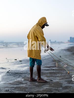 karachi pakistan 2021, un pêcheur portant une veste jaune préparant un filet de pêche pour la pêche en vue de la mer en soirée. Banque D'Images