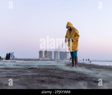 karachi pakistan 2021, un pêcheur portant une veste jaune préparant un filet de pêche pour la pêche en vue de la mer en soirée. Banque D'Images