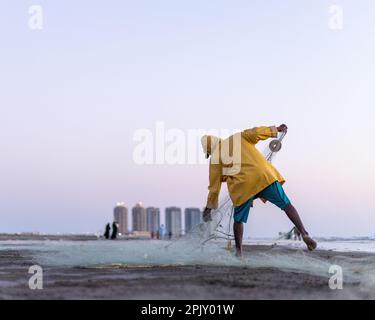 karachi pakistan 2021, un pêcheur portant une veste jaune préparant un filet de pêche pour la pêche en vue de la mer en soirée. Banque D'Images