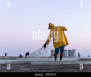 karachi pakistan 2021, un pêcheur portant une veste jaune préparant un filet de pêche pour la pêche en vue de la mer en soirée. Banque D'Images