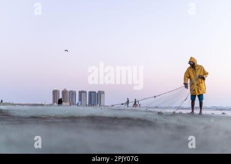 karachi pakistan 2021, un pêcheur portant une veste jaune préparant un filet de pêche pour la pêche en vue de la mer en soirée. Banque D'Images