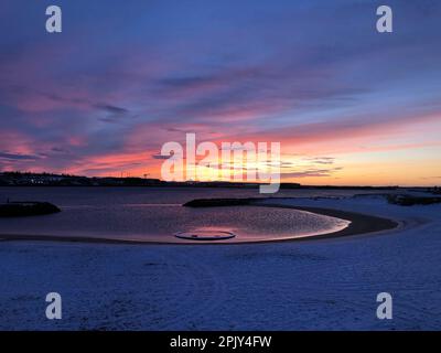 Un superbe coucher de soleil orange illumine une plage enneigée, avec le soleil au loin Banque D'Images