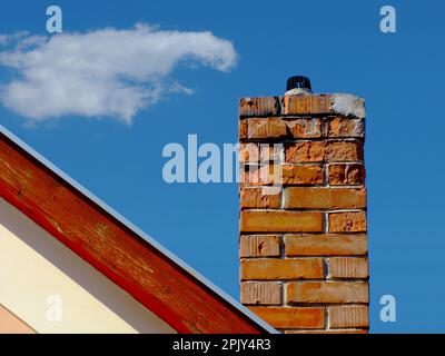 Cheminée isolée en brique d'argile qui se détériore avec une surface abîmée et écalée. garniture en bois sur le mur d'extrémité du toit de la maison. élévation extérieure en stuc blanc. Banque D'Images