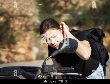 une jeune femme mignonne avec un sac à dos se regarde dans le miroir d'une moto qui ajuste ses cheveux. Photo de haute qualité Banque D'Images