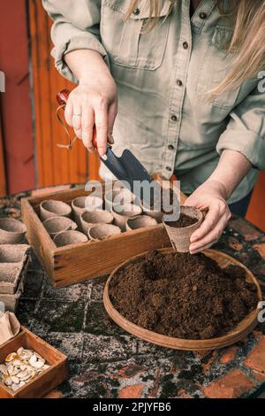 Jardinier avec pelle mettant le sol et le compost dans des pots de tourbe biodégradables. Plantation et semis au printemps Banque D'Images