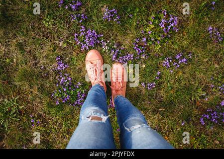 Femme portant des jeans et des sneakers roses marchant dans l'herbe avec des fleurs violettes. Saison de la mode du printemps Banque D'Images