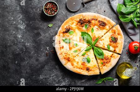 Pizza à quatre fromages sur fond sombre, pizza fraîchement cuite et feuilles de basilic Banque D'Images