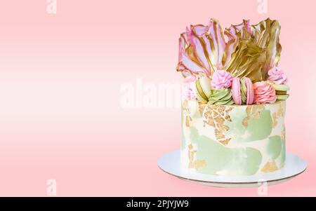 Magnifique gâteau au fromage à la crème rose et vert avec du papier de riz, de l'or comestible et des macarons. Délicieux gâteau d'anniversaire isolé. Banque D'Images