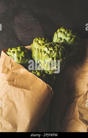 Fleurs d'artichaut vert enveloppées dans du papier kraft sur fond noir rustique en métal, vue de dessus Banque D'Images