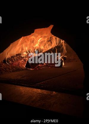 Le bois est flamboyant dans le four avec une flamme nue qui brille dans l'obscurité de la nuit Banque D'Images