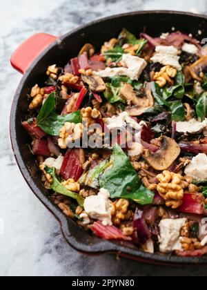 Épeautre avec du bard suisse rouge, des champignons, des noix et des feta végétaliens dans une casserole en fonte. Banque D'Images