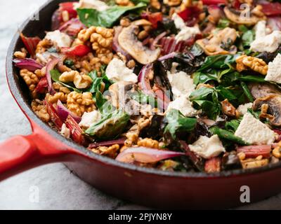 Épeautre avec du bard suisse rouge, des champignons, des noix et des feta végétaliens dans une casserole en fonte. Banque D'Images