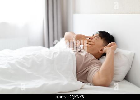 Un homme asiatique fatigué bâillonant en se réveillant dans sa chambre Banque D'Images