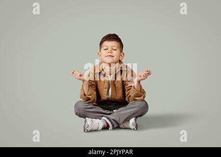 Joyeux caucasien 6 ans petit enfant dans une ambiance décontractée s'asseoir sur le sol avec espace libre isolé sur fond gris studio Banque D'Images