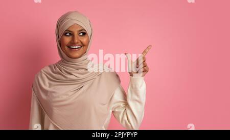 Offre agréable. Femme arabe souriante dans le hijab pointant de côté sur Copy Space Banque D'Images