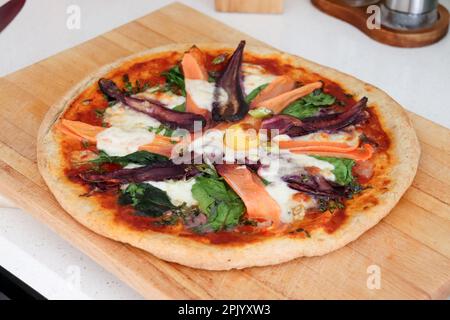 Pizza aux légumes de carottes orange et pourpre sur planche à découper en bois. Banque D'Images