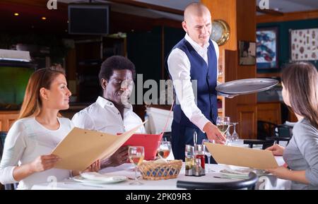 serveuse positive qui commande aux clients au café Banque D'Images