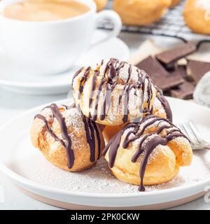 Profiteroles faits maison avec crème fouettée et garniture au chocolat, recouvertes de chocolat fondu, sur une assiette, carré Banque D'Images