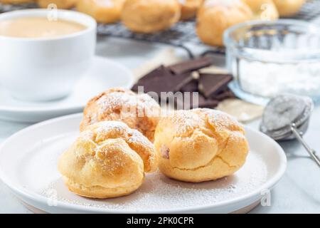 Profiteroles faits maison avec crème fouettée et garniture au chocolat, recouvertes de sucre glace, sur une assiette, horizontale Banque D'Images