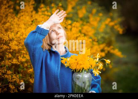 Un bouquet de fleurs jaunes sur fond de fleurs jaunes dans les mains d'une femme. Une femme d'âge moyen en manteau bleu. Banque D'Images