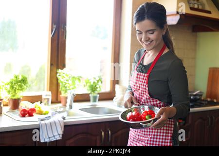 Jeune femme tenant la passoire avec des poivrons frais dans la cuisine, espace pour le texte Banque D'Images