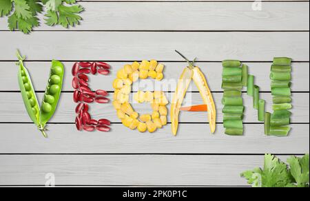 Mot VEGAN fait de différents légumes frais savoureux sur fond de bois blanc, plat Banque D'Images