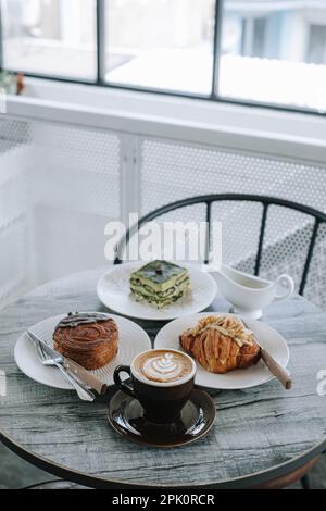 Une table avec des assiettes de boulangerie et des tasses de café. Axé sur la tasse de café. Portrait ou vertical. Petit-déjeuner le matin. Arrière-plan flou. Banque D'Images