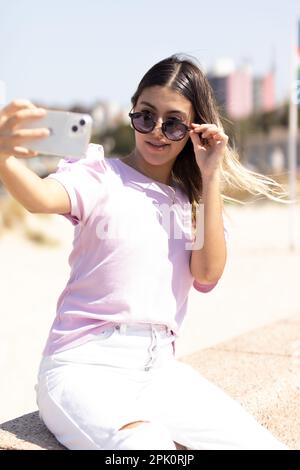 Jeune fille prenant un selfie sur la Rambla à Montevideo. Il abaisse ses lunettes sombres pour poser Banque D'Images