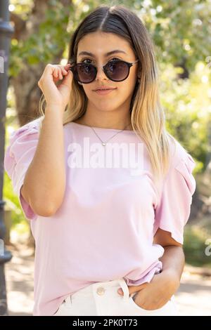 Adolescente regardant ses lunettes sombres à l'appareil photo. Banque D'Images