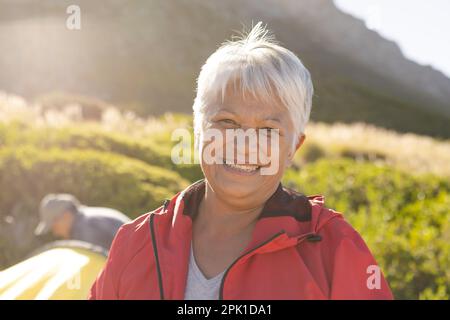 Portrait d'une heureuse femme biraciale senior regardant l'appareil photo et souriant dans les montagnes Banque D'Images