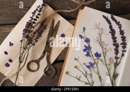 Vieux ciseaux avec de belles fleurs séchées et livre sur table en bois, plat Banque D'Images