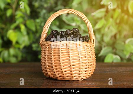 Mûres mûres de mûres de mûres noires dans un panier en osier sur une table en bois sur fond flou Banque D'Images