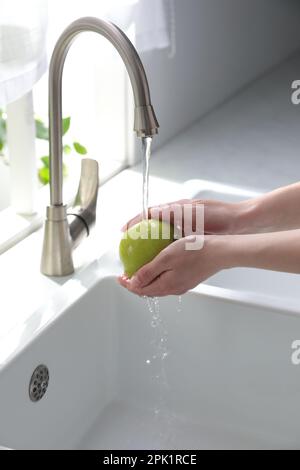 Femme lavant la pomme sur l'évier dans la cuisine, gros plan Banque D'Images