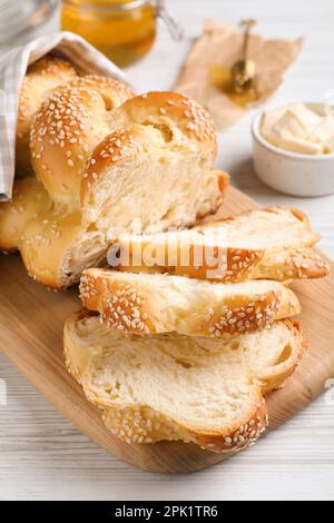 Couper du pain tressé fraîchement cuit sur une table en bois blanc, en gros plan. Challah traditionnel de Shabbat Banque D'Images