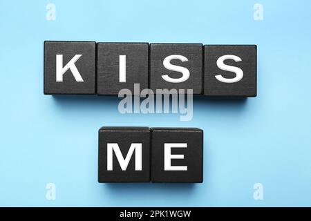 Cubes en bois noir avec l'expression Kiss Me sur bleu clair, plat Banque D'Images