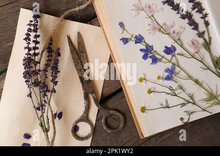 Vieux ciseaux avec de belles fleurs séchées et livre sur table en bois, plat Banque D'Images