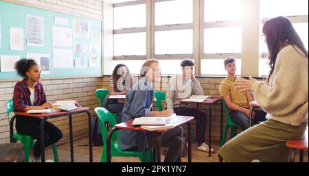 Comment se passe-t-il aujourd'hui ? un jeune enseignant joyeux donnant la classe à un groupe d'enfants d'école à l'intérieur d'une école pendant la journée. Banque D'Images