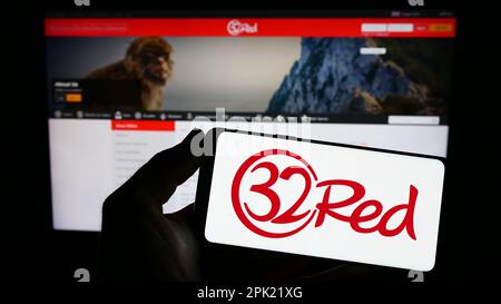 Personne tenant un smartphone avec le logo de la compagnie de casino en ligne 32Red Limited sur l'écran devant le site Web. Mise au point sur l'affichage du téléphone. Banque D'Images