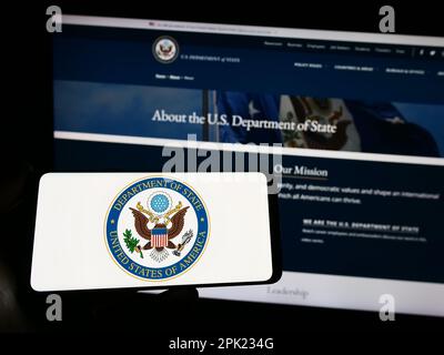 Personne tenant un smartphone avec le sceau du Département d'État des États-Unis (DOS) sur l'écran devant le site Web. Mise au point sur l'affichage du téléphone. Banque D'Images