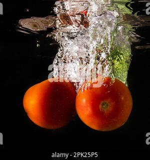 Tomate mûre tombe profondément sous l'eau avec un grand bruit. Banque D'Images