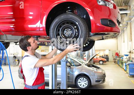 Mécanicien automobile professionnel travaille dans un atelier et réparations véhicules - vérifier la technologie, freins et pneus Banque D'Images