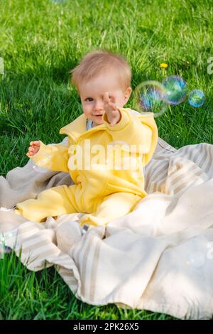 Assis sur une couverture, un enfant éclate des bulles dans le parc Banque D'Images